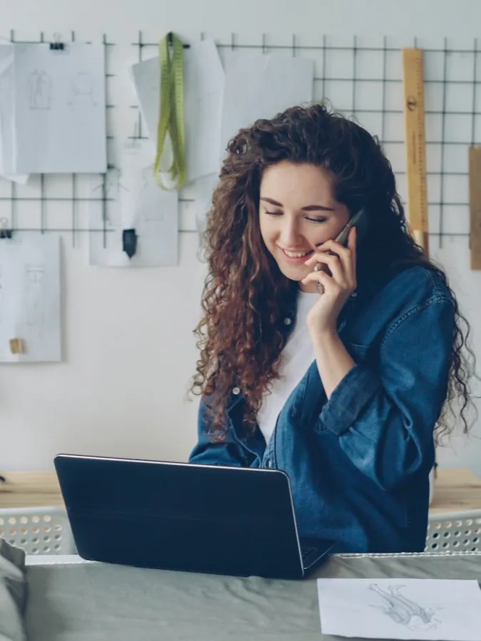 A shop owner mid call at her workbench, laptop open, taking the question in real time