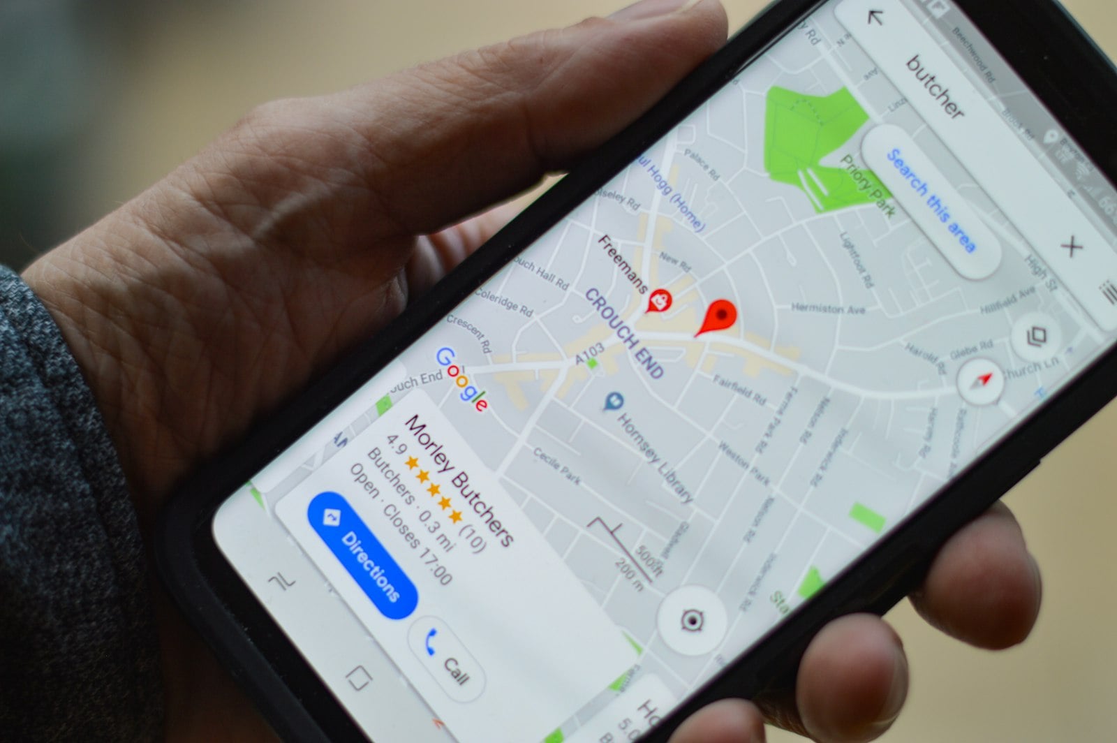 Hand holding a phone showing a Google Maps search for a local business, with the top result carrying five stars and call and directions buttons