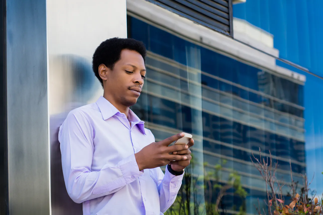 Man in a dress shirt looks something up on his phone outside an office building