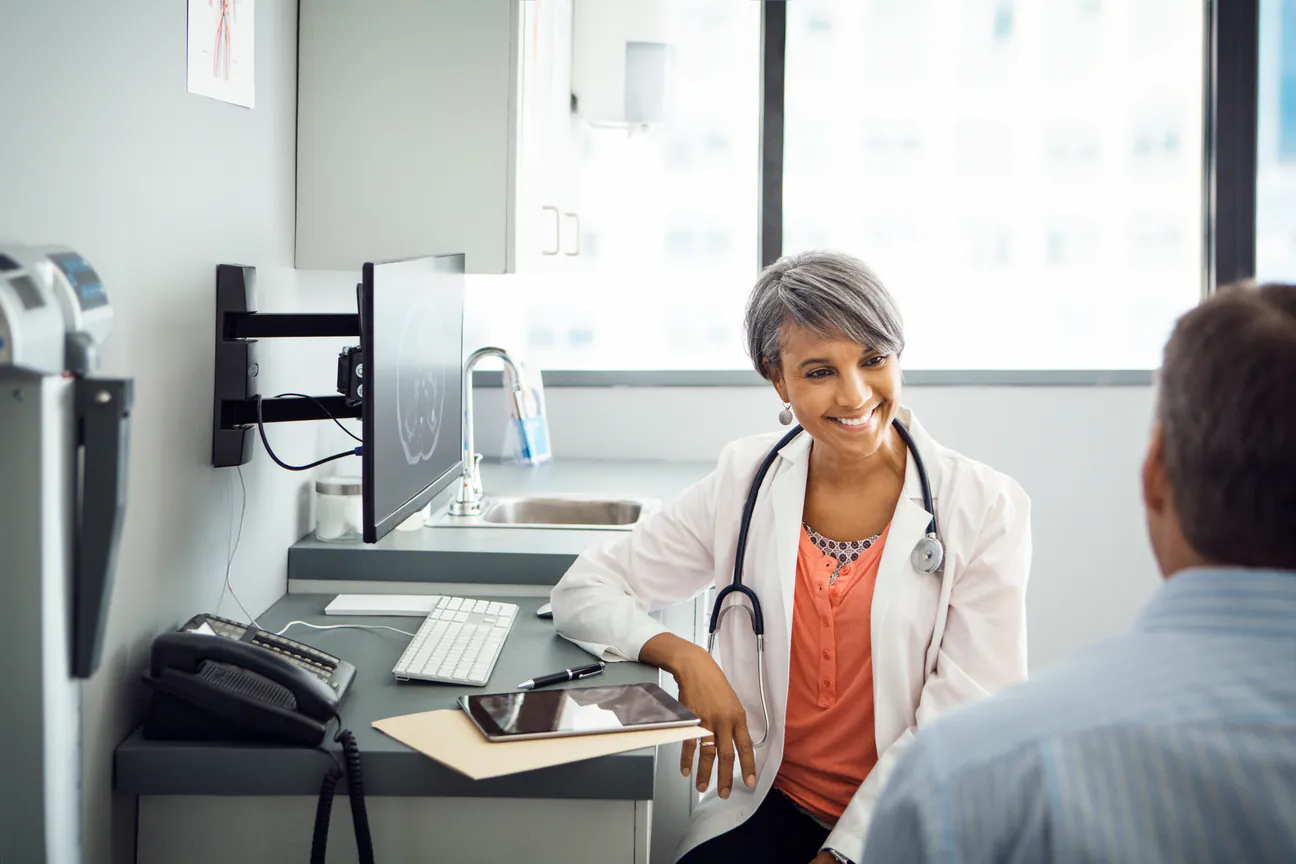 Doctor in a white coat talks with an adult patient in her exam room